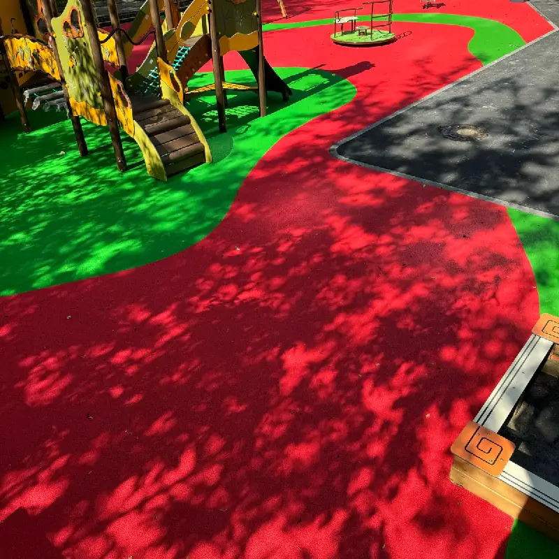 Red and green EPDM rubber playground surface with tree shadows.